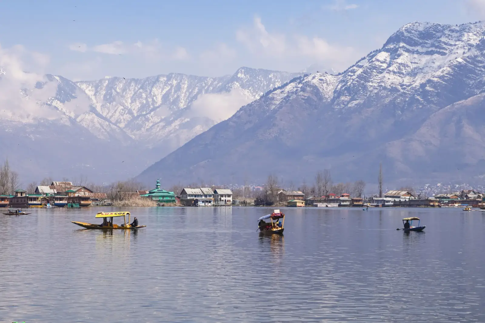 Dal Lake in Srinagar with shikaras on calm water and snow-capped mountains rising behind the lakeside