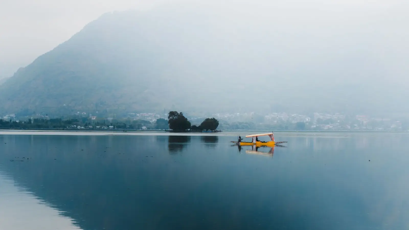 A shikara crossing a calm, misty Dal Lake in Srinagar