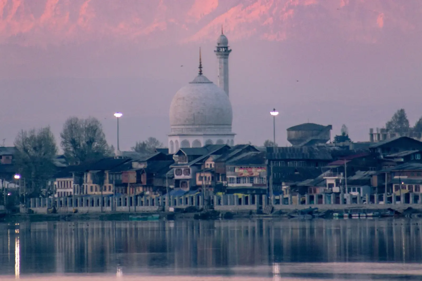 The white dome and minaret of Hazratbal shrine above lakeside houses on Dal Lake, Srinagar, under a pink evening sky
