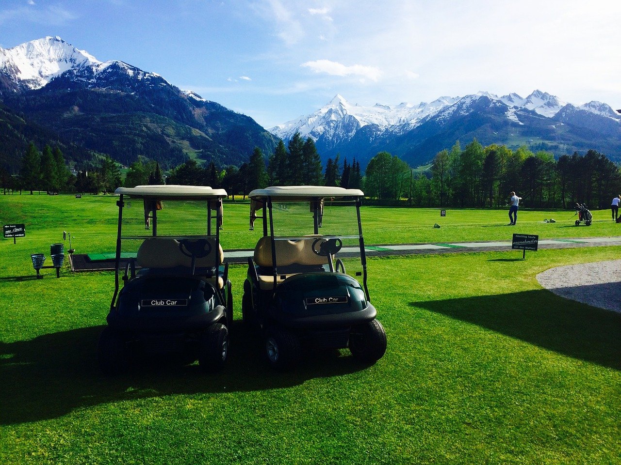 Golf carts parked on a green fairway with snow-capped mountains in the background