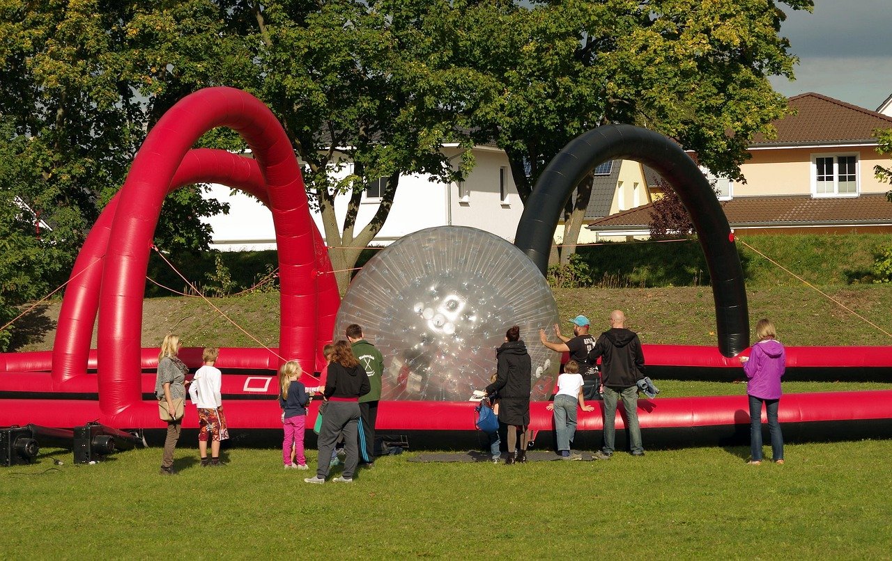 A large inflatable zorb ball with people gathered around it on a grassy field