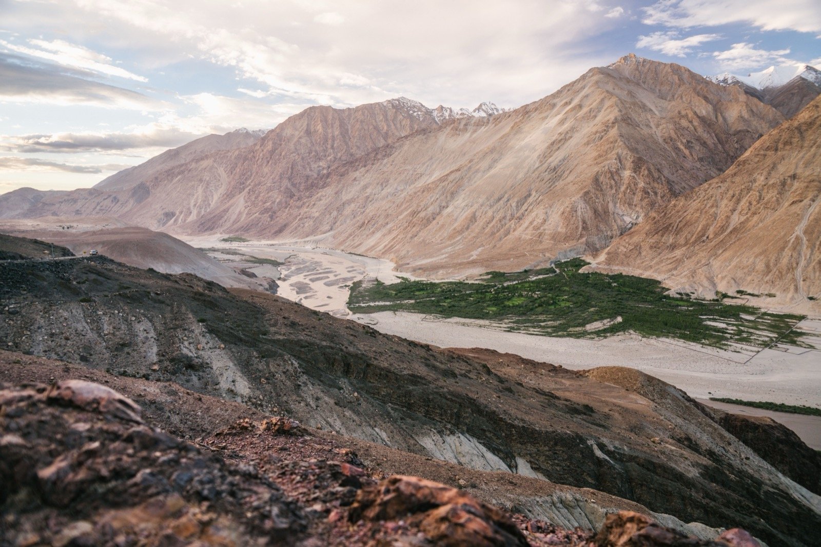 The Nubra Valley in Ladakh - a green river oasis of fields and poplar trees running through a wide brown high-desert valley, framed by bare mountains with snow on the distant peaks