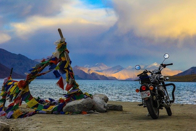Pangong Tso lake at sunset with prayer flags on the shore and mountains reflecting warm light on the far side