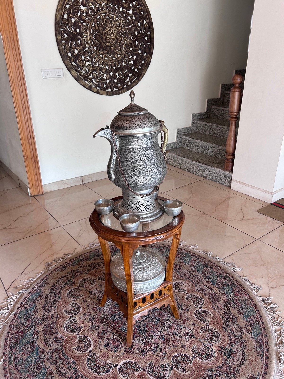 A Kaalai craftsman in Mohalla Thokurs working at a copper samovar -- the beaten surface visible, tools laid out on the work mat, the narrow lane of the Old City visible through the workshop door