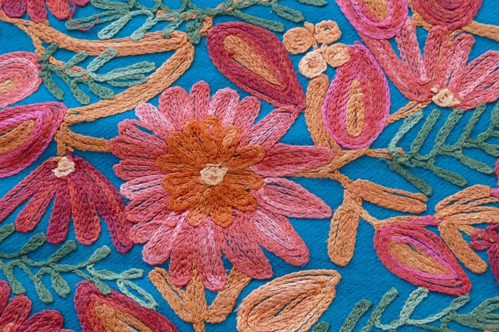 Close-up of Kashmiri embroidery in progress -- fine needle stitching a floral vine motif in coloured silk thread on cream Pashmina