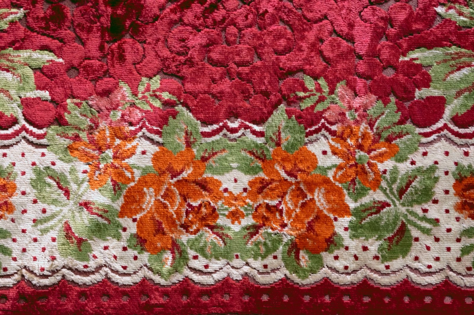 A craftsman in a Sopore workshop pressing and rolling a half-finished Namda on a flat floor -- the wool mat visibly compressed and beginning to hold shape, wooden rollers beside it, finished embroidered pieces hanging on the wall behind
