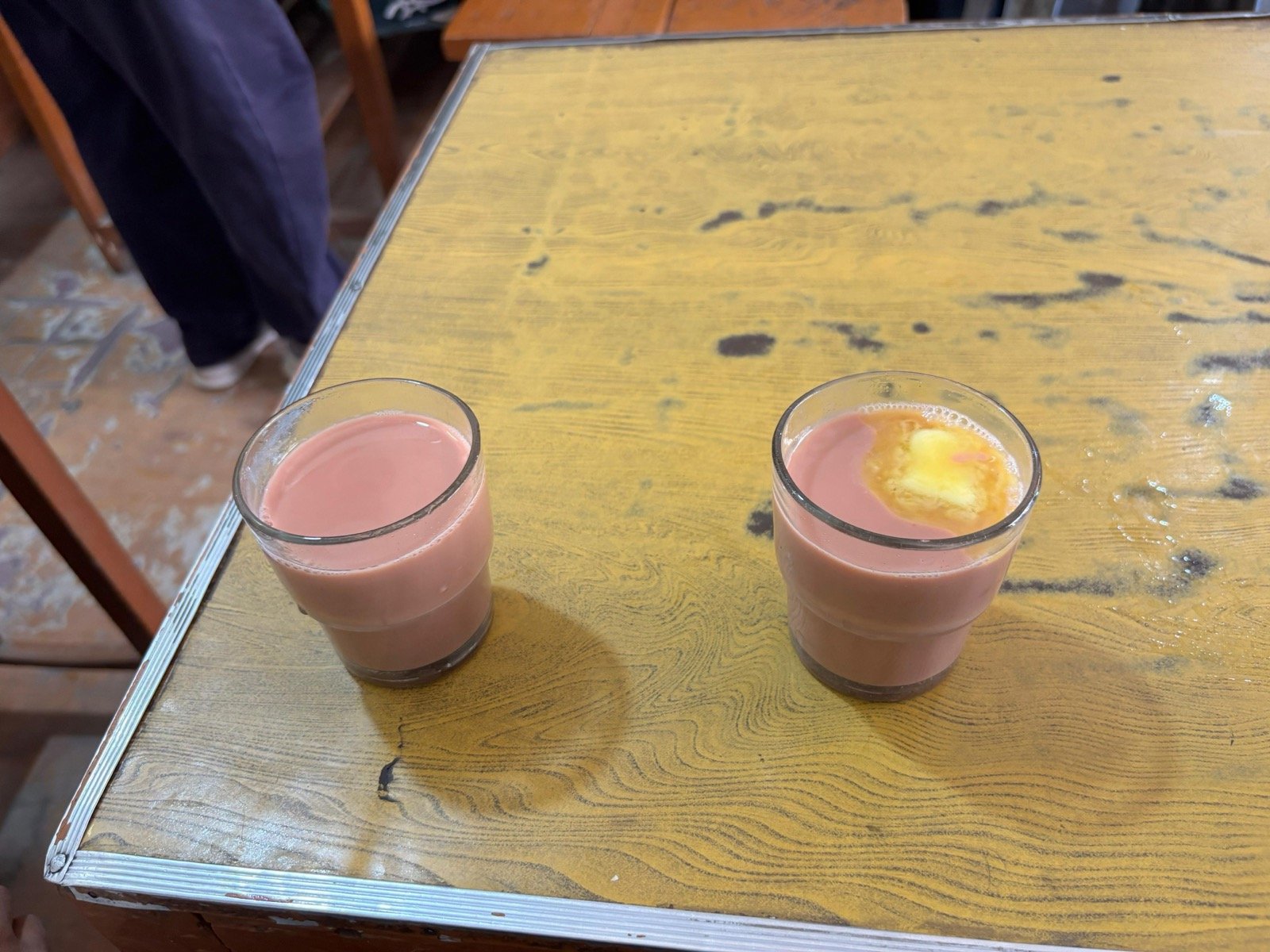 A white ceramic cup of noon chai - dusty pink, slight cream swirl on top - on a wooden surface with torn girda bread beside it, morning window light
