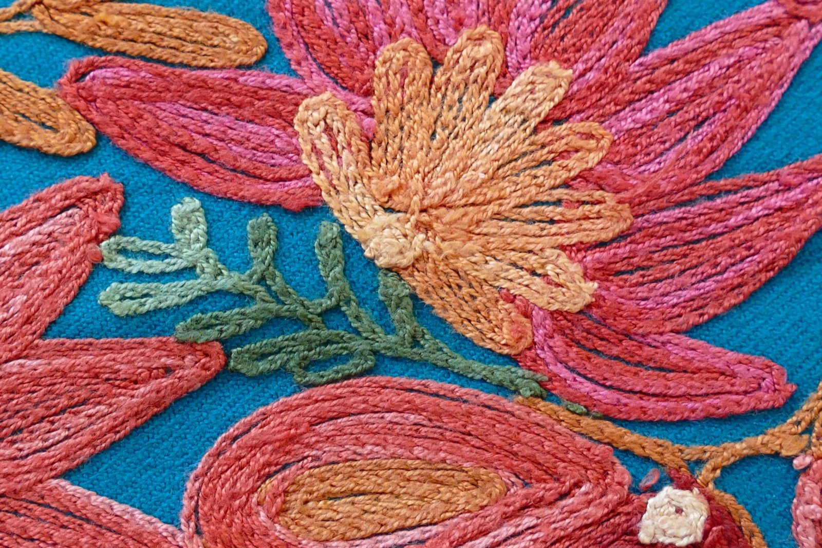 Close-up of Kashmiri Sozni embroidery in progress - fine needle stitching a floral vine motif in blue silk thread on cream Pashmina