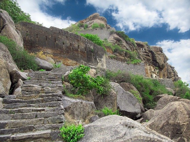 The main temple ruins at Naranag, carved stone base visible, the Wangath Nallah running in the foreground, forested hillside behind