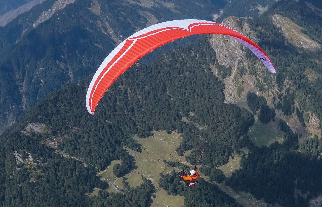 Paraglider with a red-and-white wing over forested hills