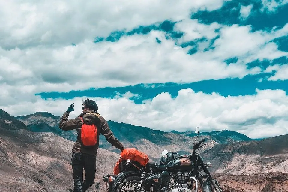 A rider seen from behind beside a Royal Enfield on a mountain road in Ladakh