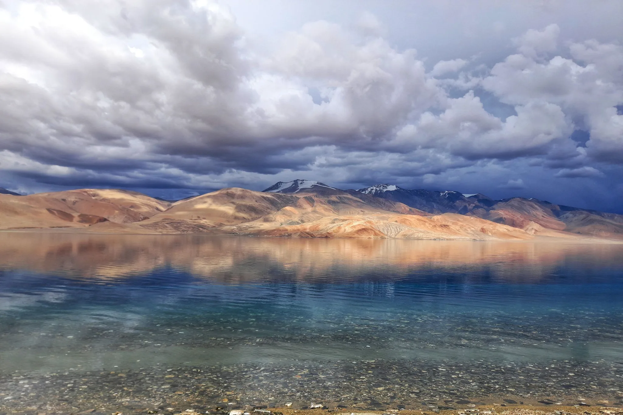 Tso Moriri lake reflecting golden mountains and storm clouds, Changthang, Ladakh